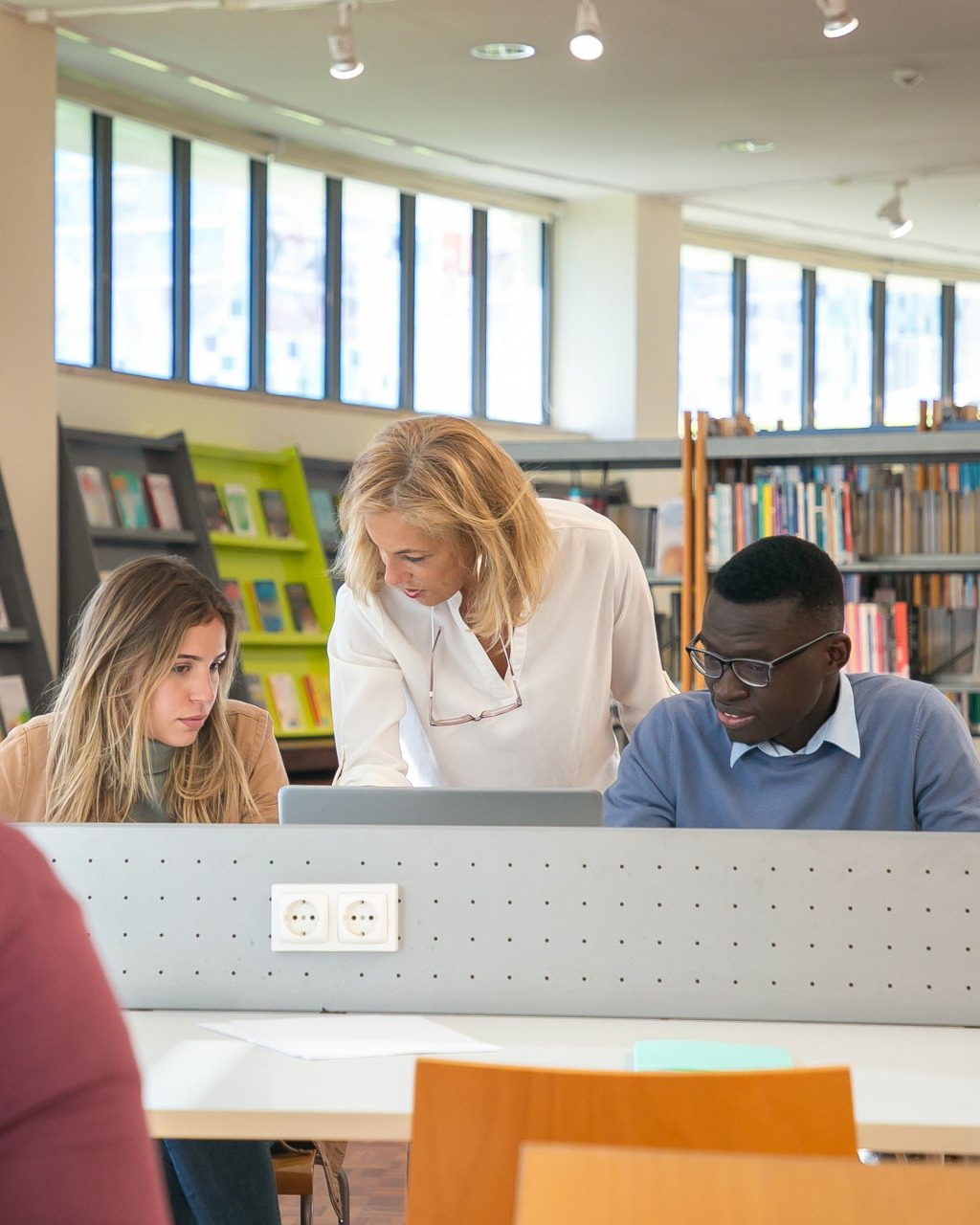 Students and a teacher working together at a laptop in a library study area