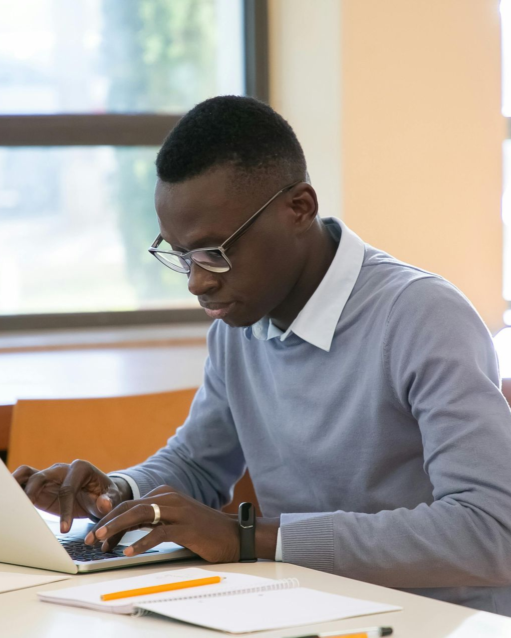 Person using a laptop and writing in a notebook at a desk indoors