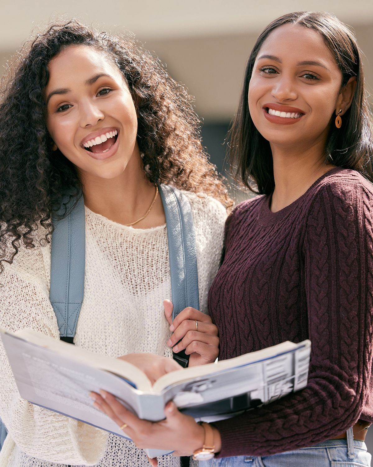 Students in a classroom. Some smiling and looking toward a person in front. Desks, window, bright lighting.