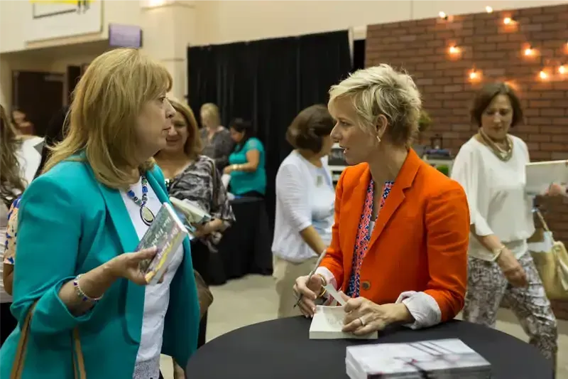 Two women are sitting at a table talking to each other.