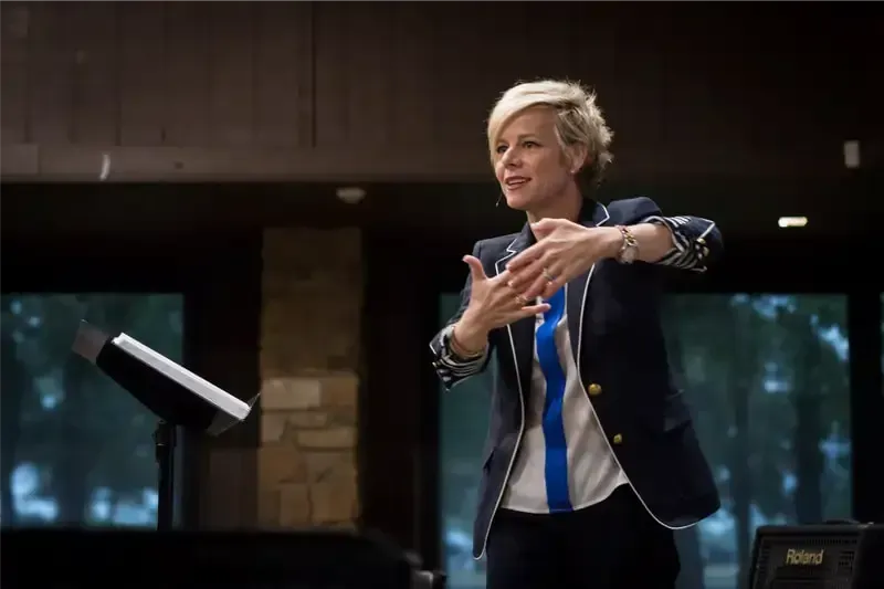 A woman in a suit and tie is giving a speech at a podium.