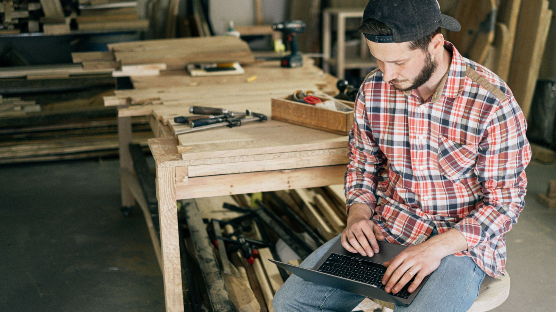 A tradie in a plaid shirt using a laptop to review his local SEO in a woodworking workshop, surrounded by tools