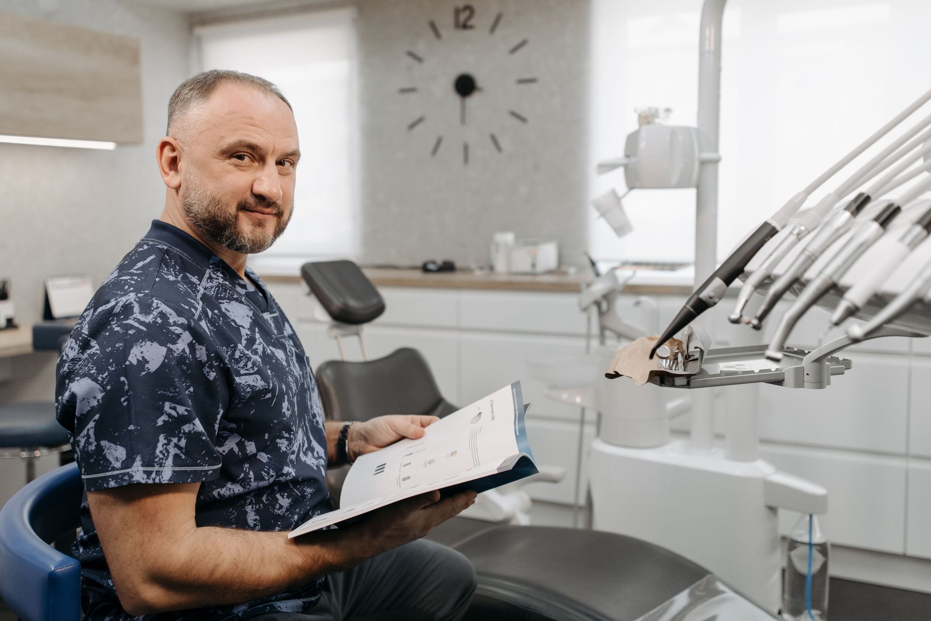 Local Dentist in navy scrubs holding a clipboard beside a dental chair and treatment equipment deciding on app strategy