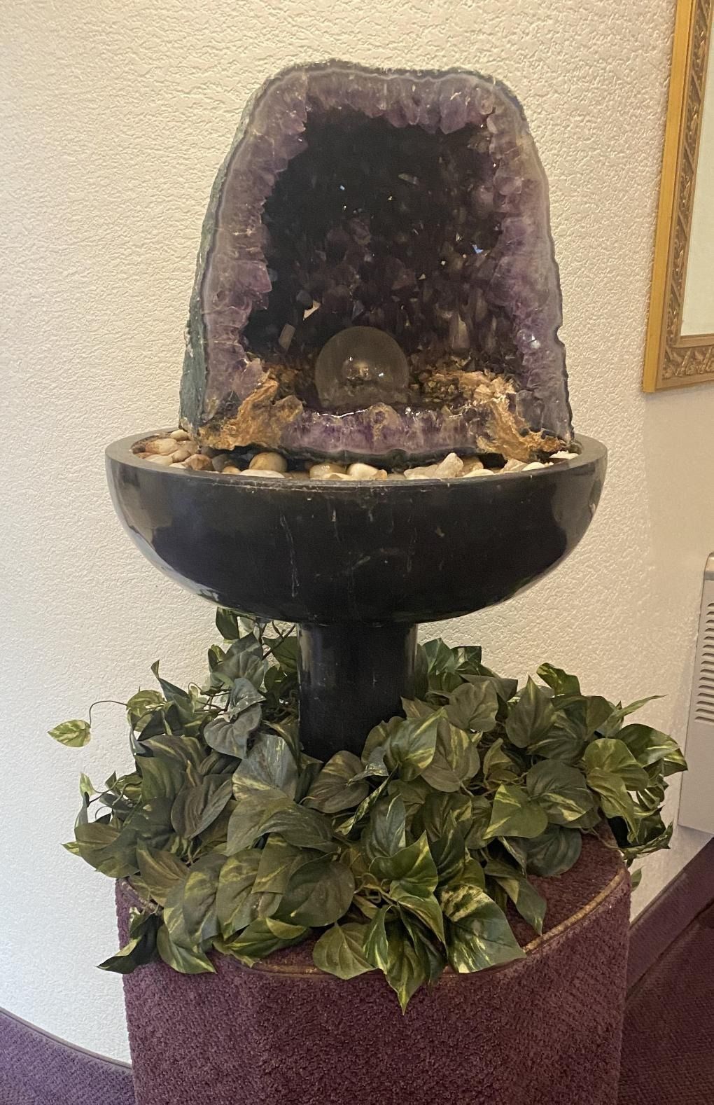 Decorative black fountain with purple geode top and ivy at the base indoors