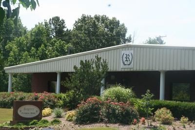 Single-story brick building with landscaped shrubs and trees in front under a bright sky
