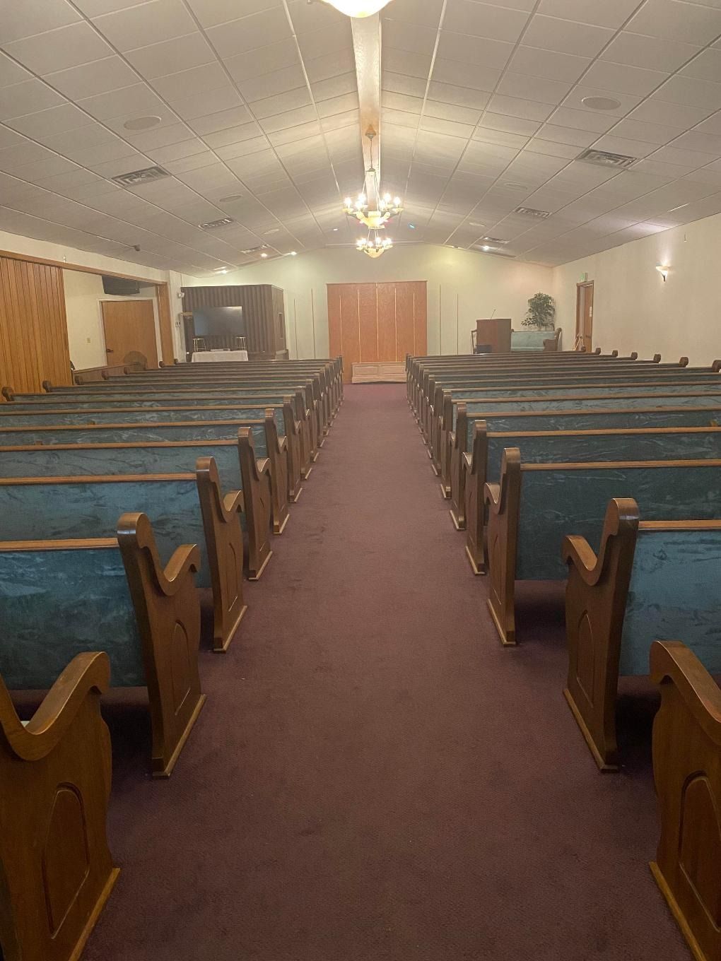 Empty church sanctuary with wooden pews, red carpet aisle, and ceiling lights leading to the altar