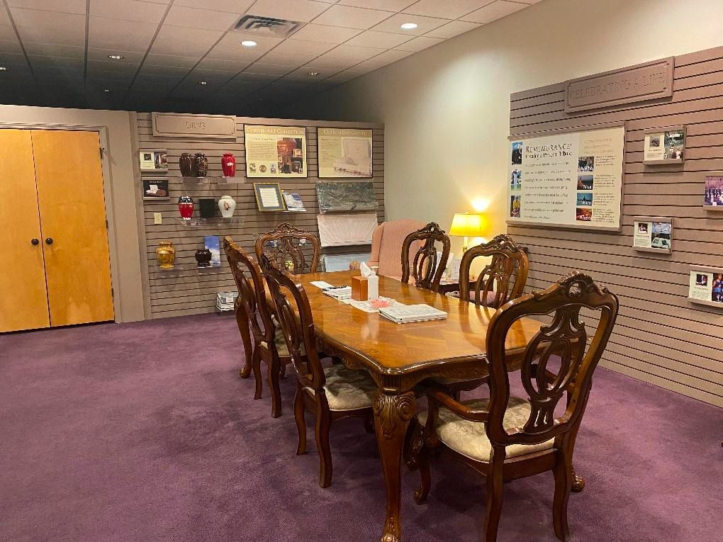 Conference room with wooden table and chairs on a purple carpet, brochure wall displays, and a glowing lamp.