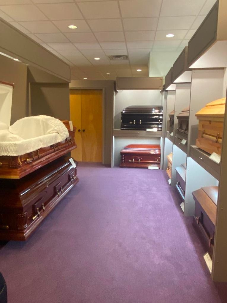 Funeral home room with two open caskets, purple carpet, and wood-paneled walls