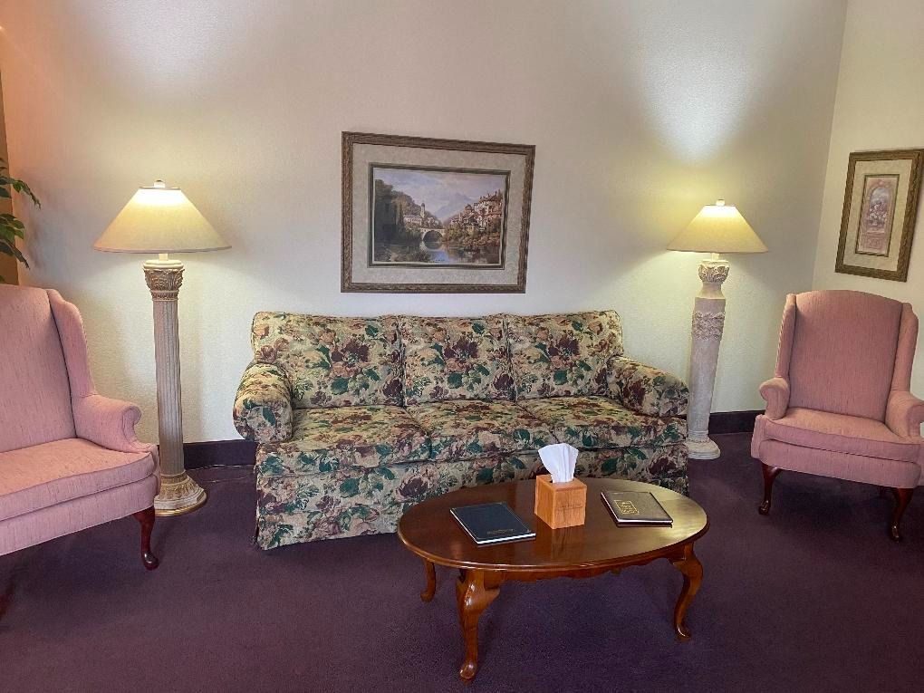 Cozy living room with floral sofa, pink chairs, lamps, framed art, and a wooden coffee table.