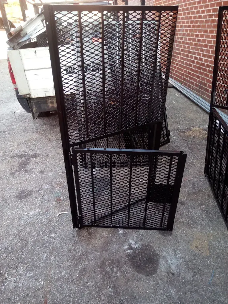 A black metal gate with a diamond mesh pattern stands upright on a concrete surface next to a parked truck.