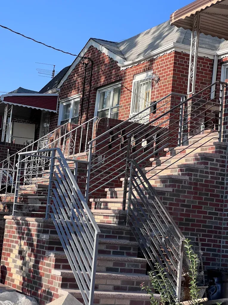 A red brick house exterior featuring a central staircase with silver metal railings leading to an elevated entrance.