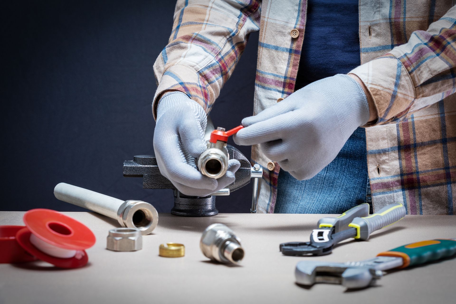Plumber wearing gloves works on a valve with tools and parts on a wooden surface.