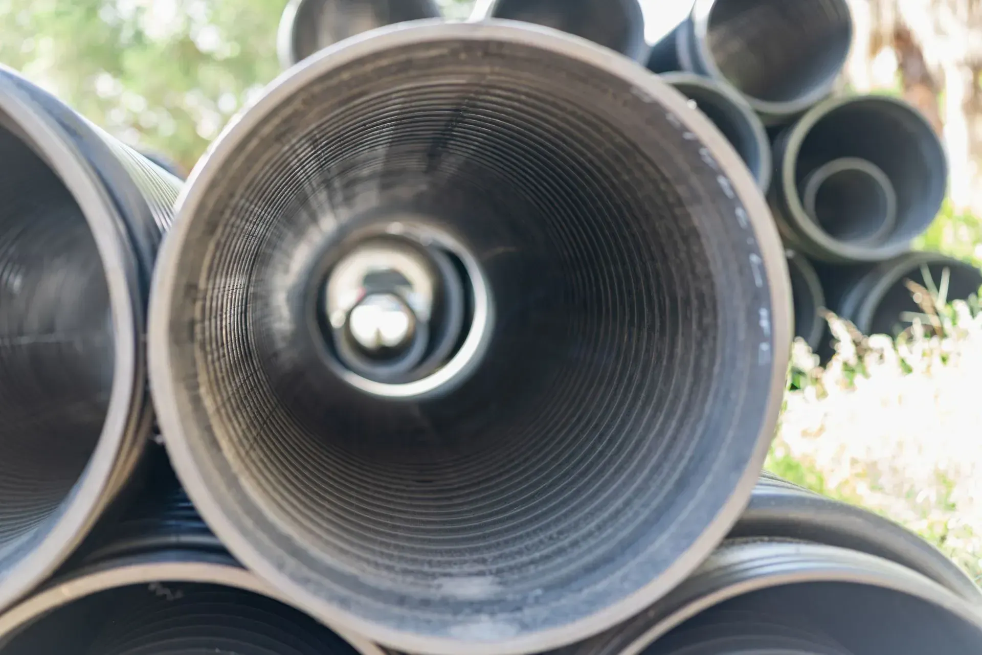 Stack of black corrugated pipes, viewed from inside one, showing concentric circles and a dim interior.