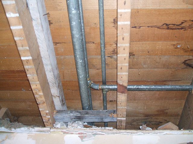 Overhead view inside a building's frame, showing plumbing pipes running through wooden beams and framing.