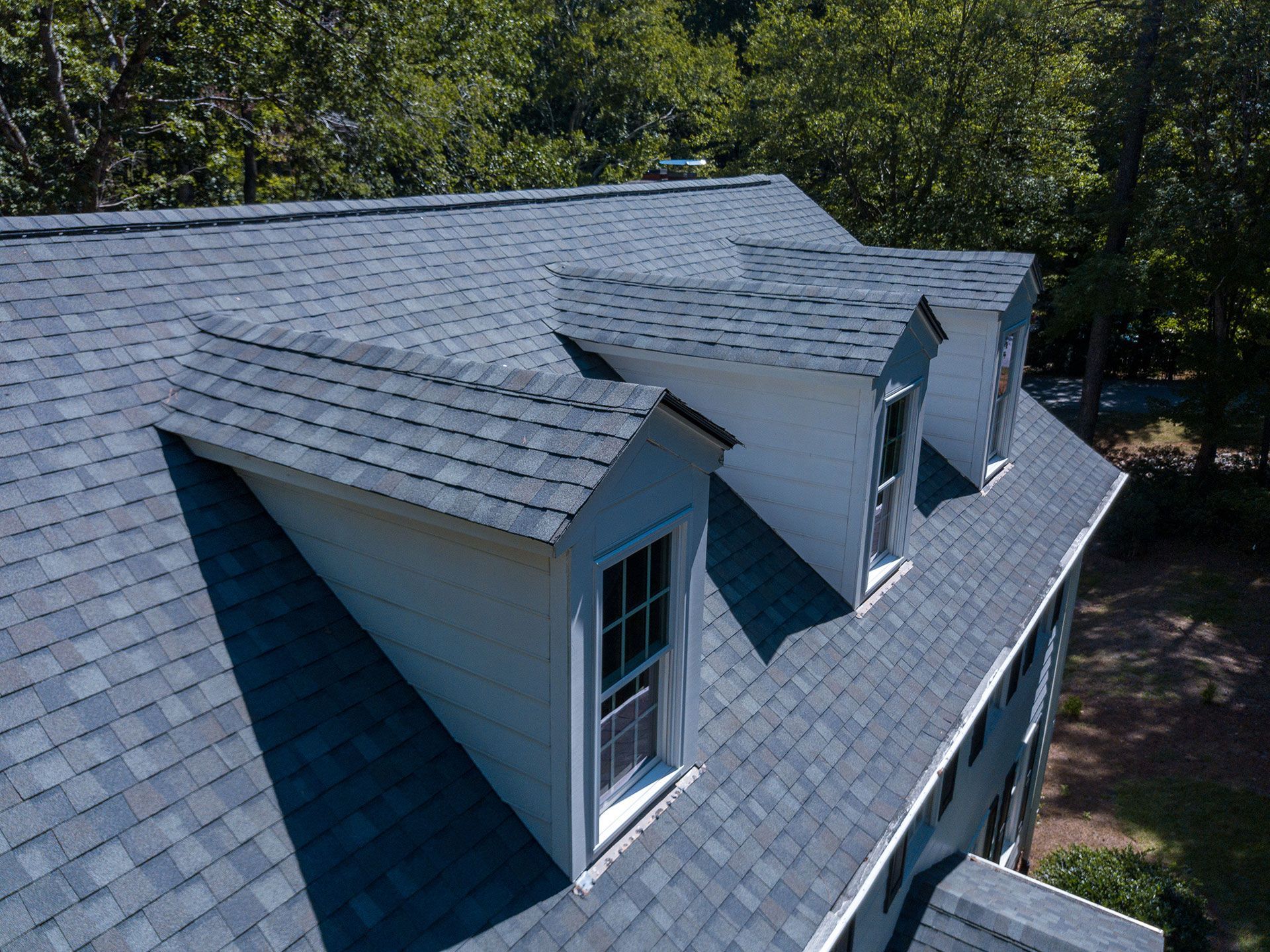 Gray asphalt shingle residential roof with dormer windows on a two-story home