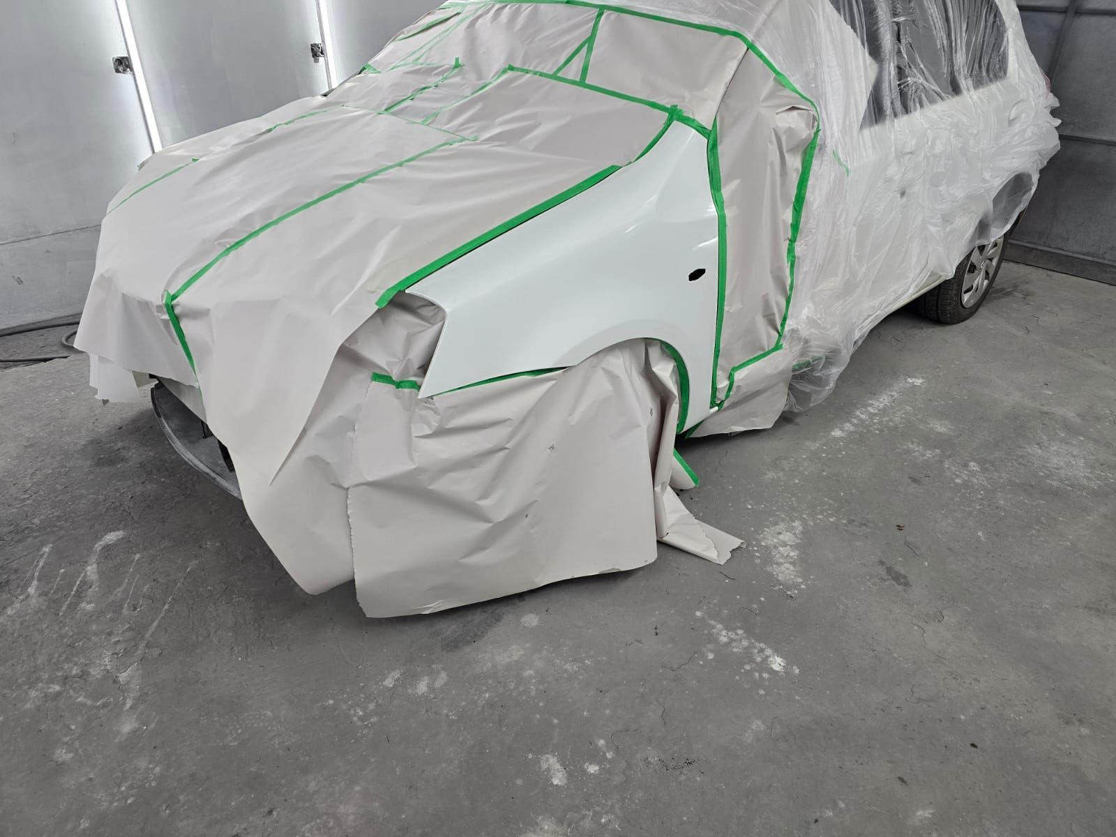 Mecánico con mono azul trabajando en la carrocería de un coche plateado en una cabina de pintura.