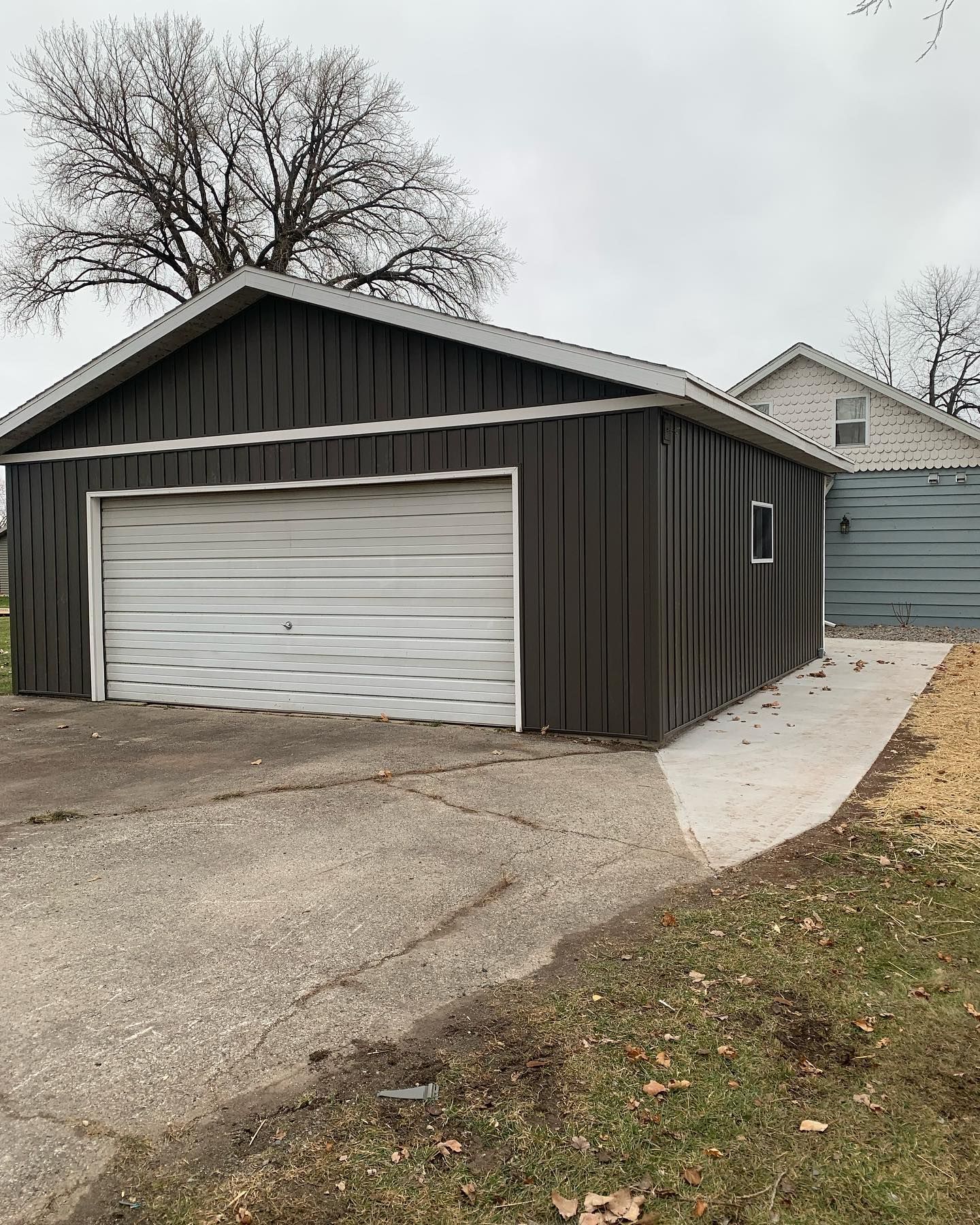 A black garage with a white door is next to a house.