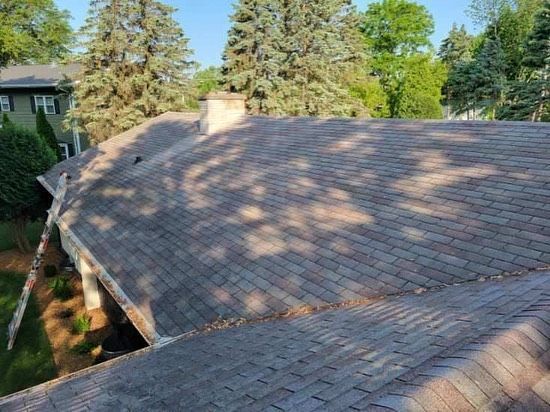 A roof of a house with a chimney and trees in the background.