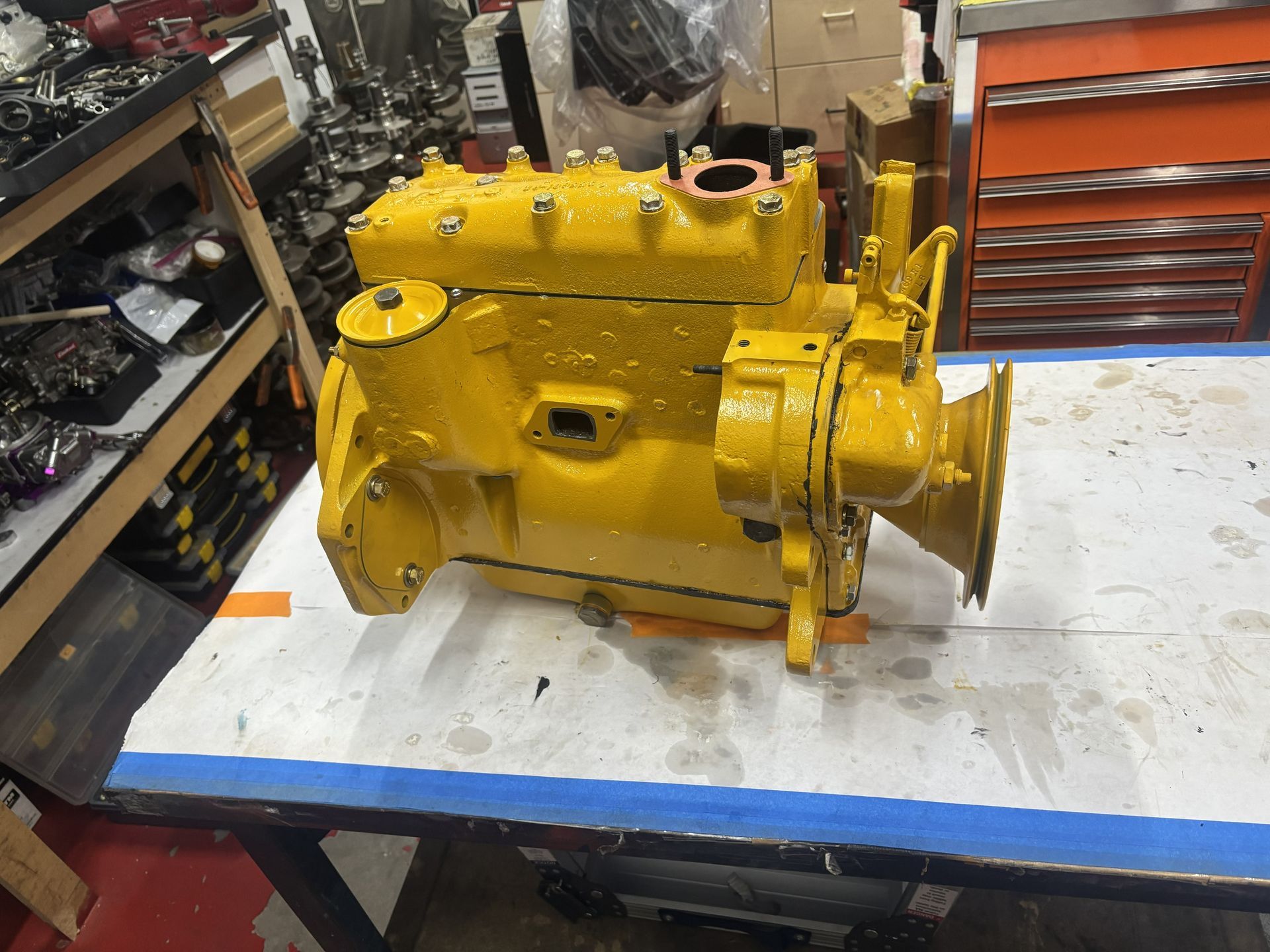 Yellow engine on a worktable. Mechanical parts and tools are in the background, workshop setting.
