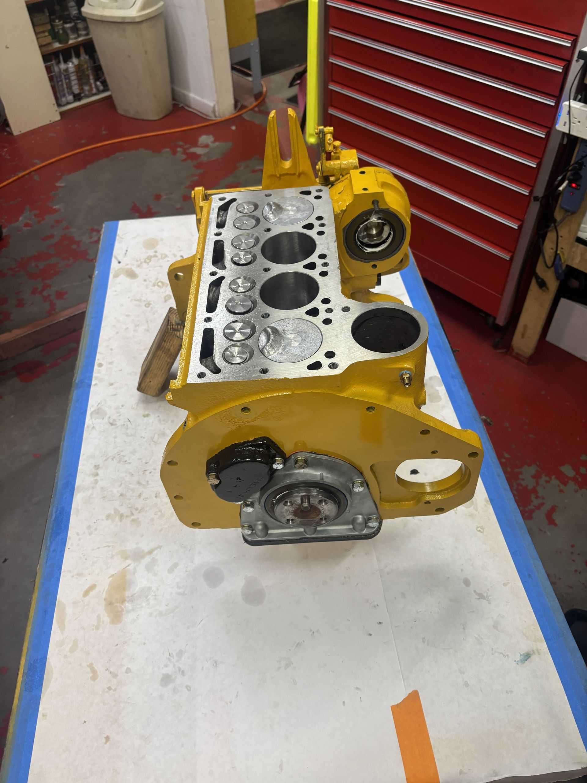 Yellow engine block on a white surface, with multiple cylinder holes visible.