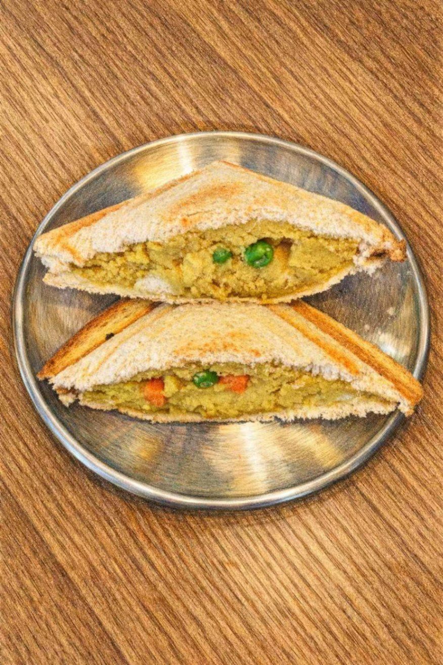 Two toasted, triangular vegetable sandwiches on a round metal plate set against a wooden table.