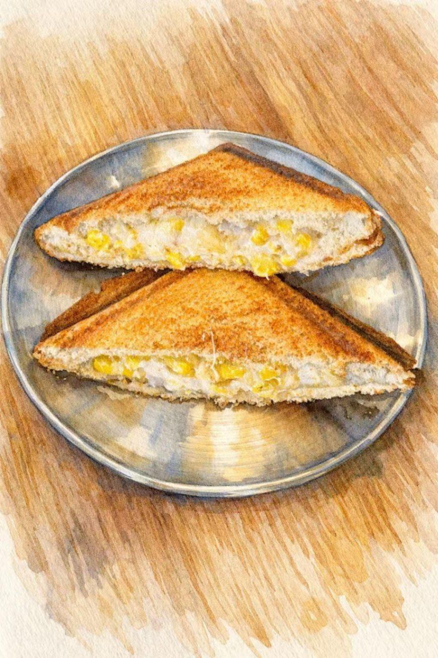Two toasted triangular corn and cheese sandwiches served on a small metallic plate over a wooden surface.