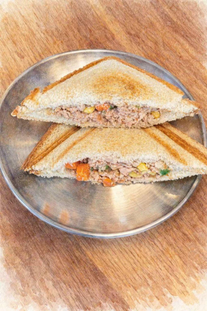 Two toasted triangular tuna sandwiches served on a round silver plate over a wooden surface.