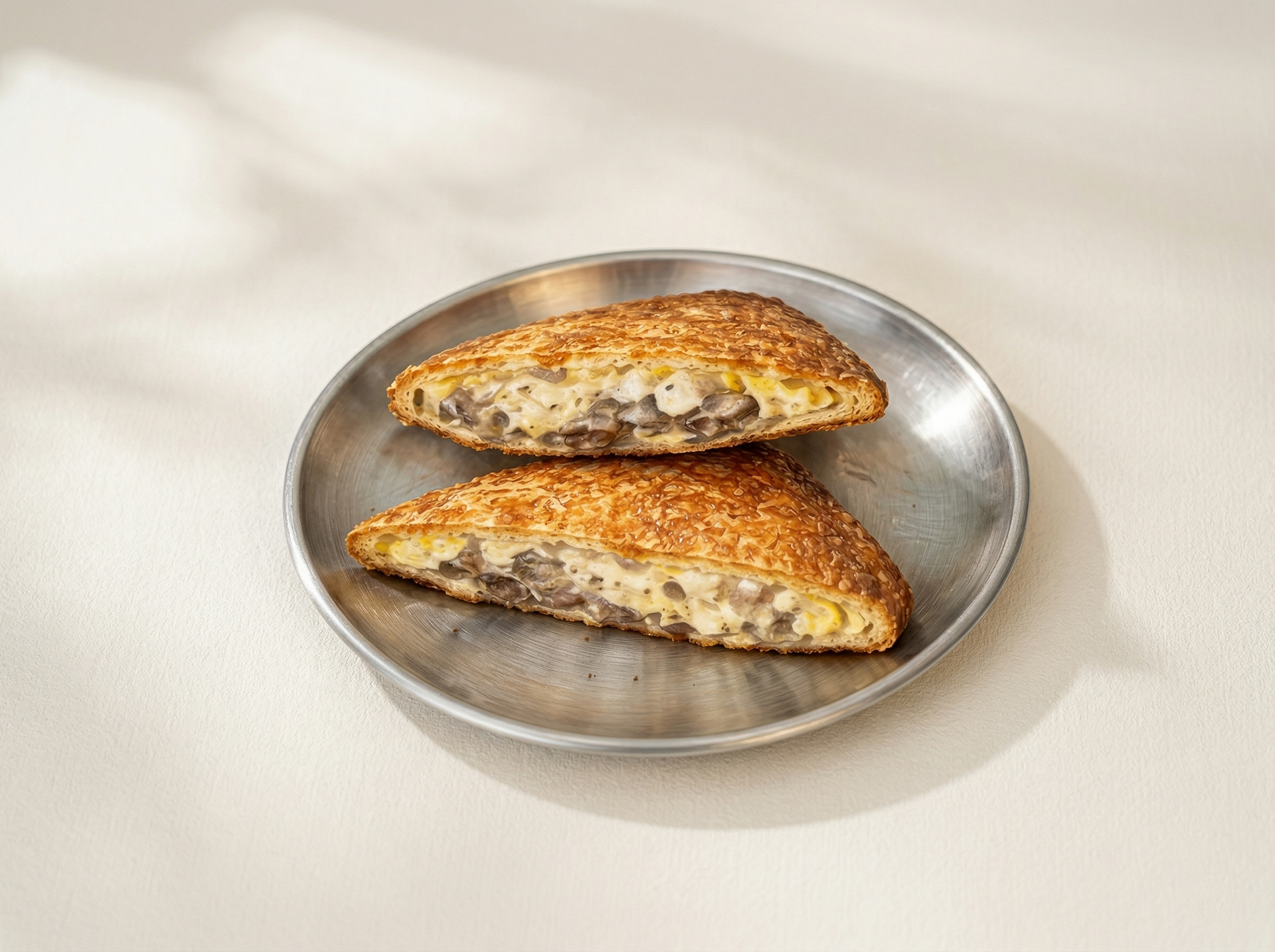 Two halves of a golden-brown toasted sandwich with a creamy, textured filling sit on a round metal plate.