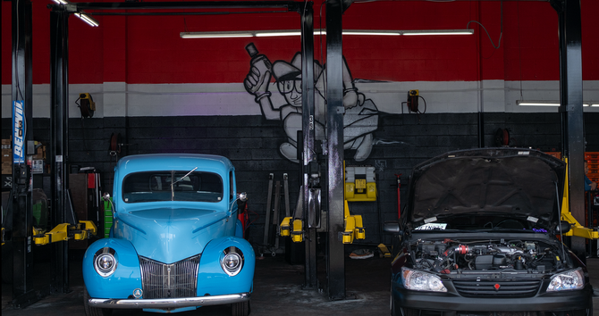 Blue vintage car and black car with open hood inside a garage.