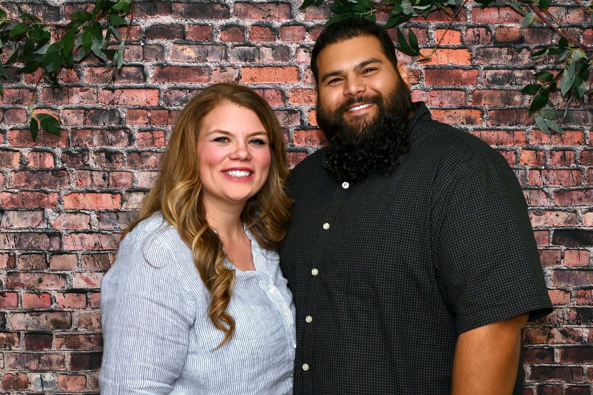 A man and a woman are posing for a picture in front of a brick wall.