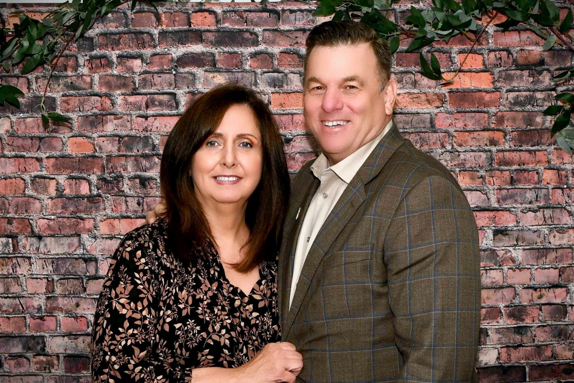 A man and a woman are posing for a picture in front of a brick wall.