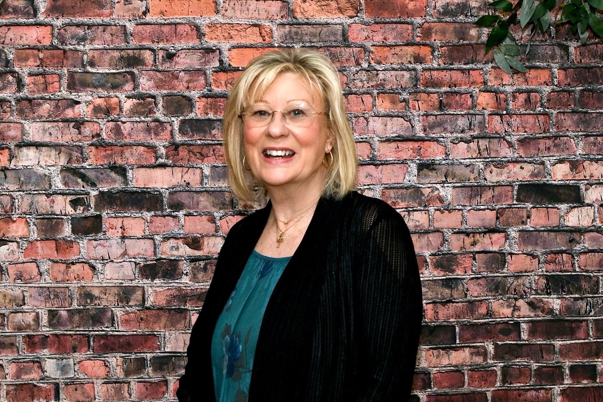 A woman is smiling in front of a brick wall.