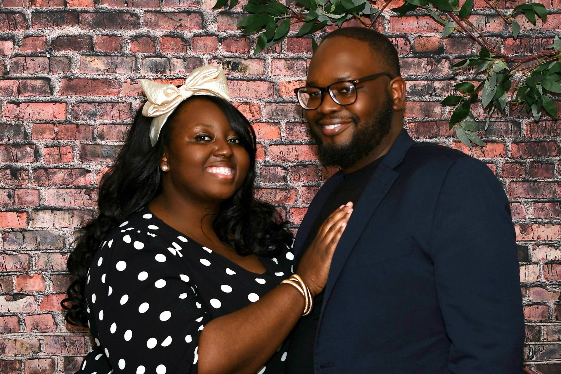 A man and a woman are posing for a picture in front of a brick wall.