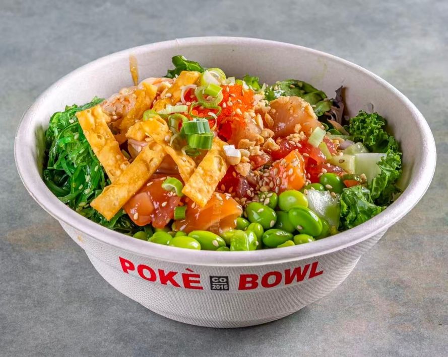 A bowl of noodle salad topped with orange roe, served on a table with stacked plates nearby.