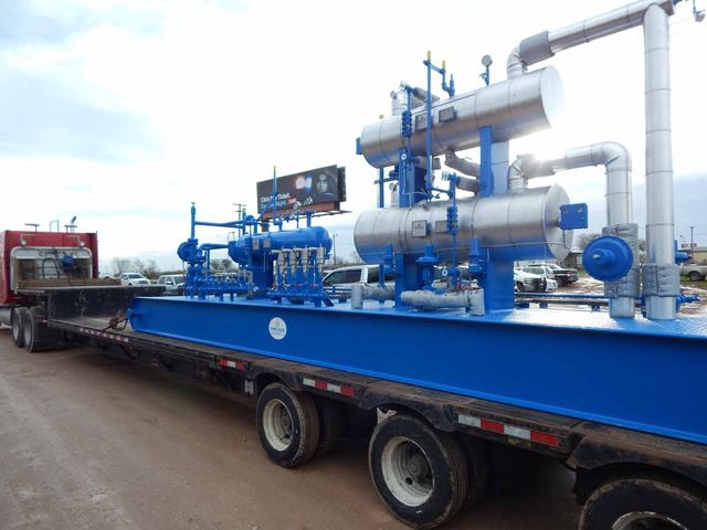 A blue semi truck is carrying a large piece of equipment.