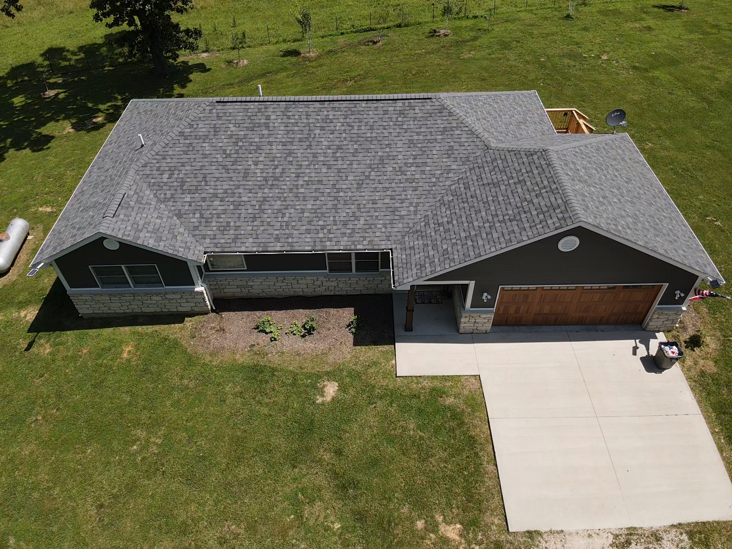 Aerial view of a gray-roofed house with a concrete driveway and green lawn.