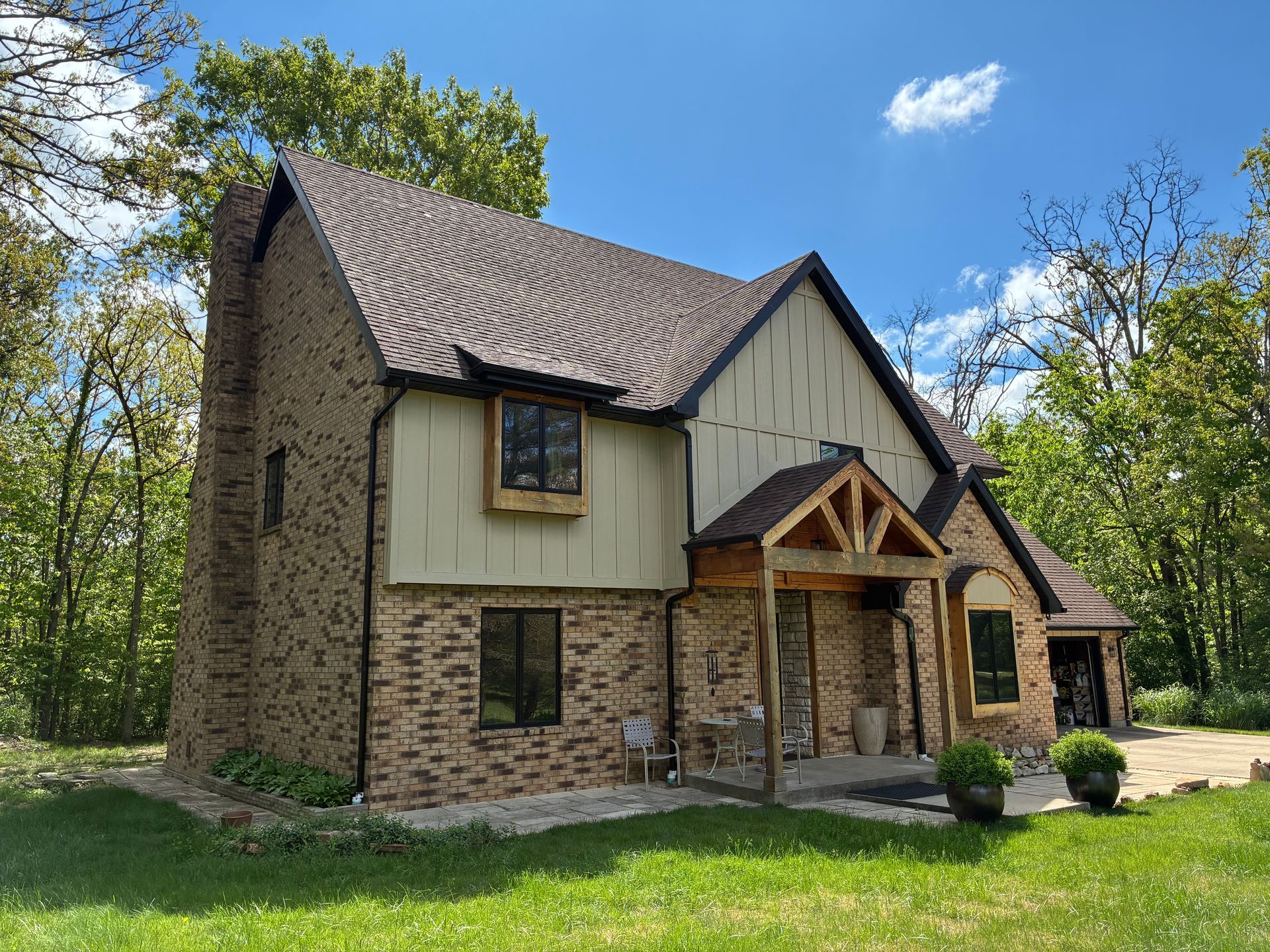 Two-story house with brick and tan siding, brown roof, and small front porch under a blue sky.
