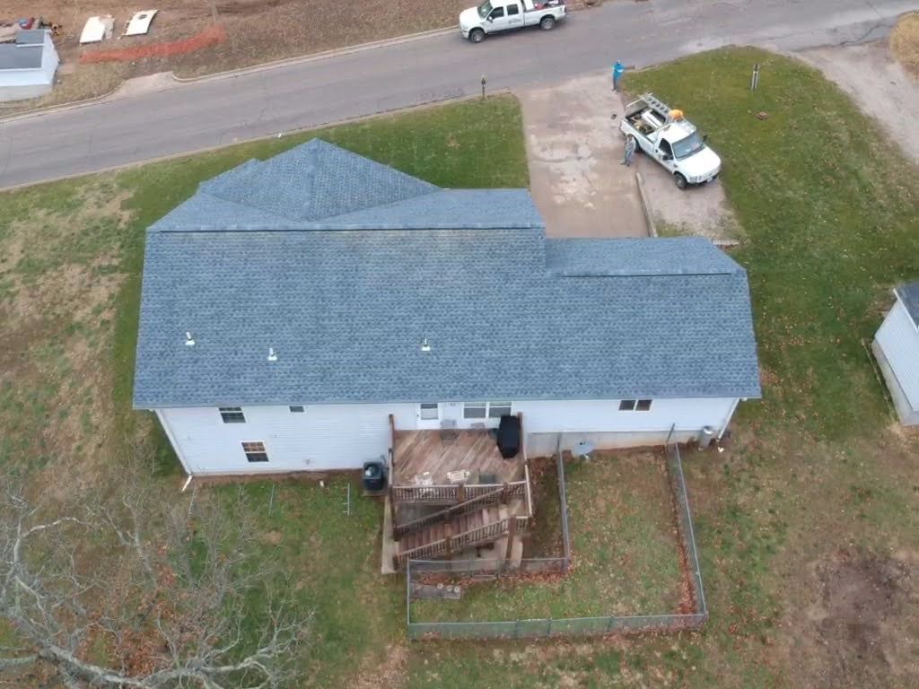 Aerial view of a white house with a gray roof and a wooden deck. Two white trucks are parked nearby.