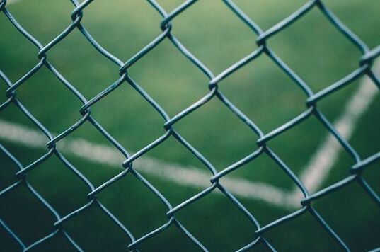 Close-up of a green chain-link fence with blurred grass in the background