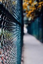 Blurred chain-link fence along a narrow path, with blue and orange tones in the background
