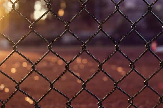 Chain-link fence with blurred warm lights in the background at dusk