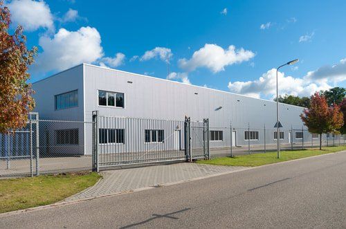 Modern industrial building with metal fence, paved road, and blue sky with clouds