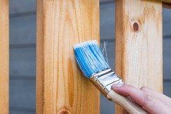 Brush applying blue paint to a wooden fence post