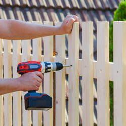 A man attaching wood fence pickets to a stringer