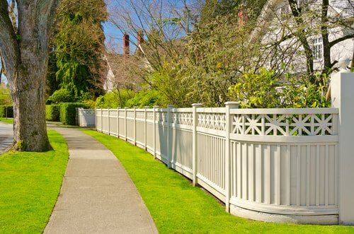 Curving sidewalk beside a white fence and green lawn on a sunny residential street