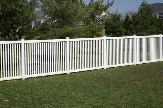 White vinyl fence bordering a green lawn with trees in the background