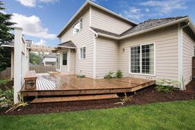 Backyard deck beside beige house with sliding doors and green lawn