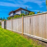 Wooden fence along a green lawn beside a modern house under a blue sky