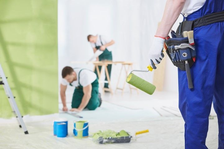 A group of men are painting a wall in a room.