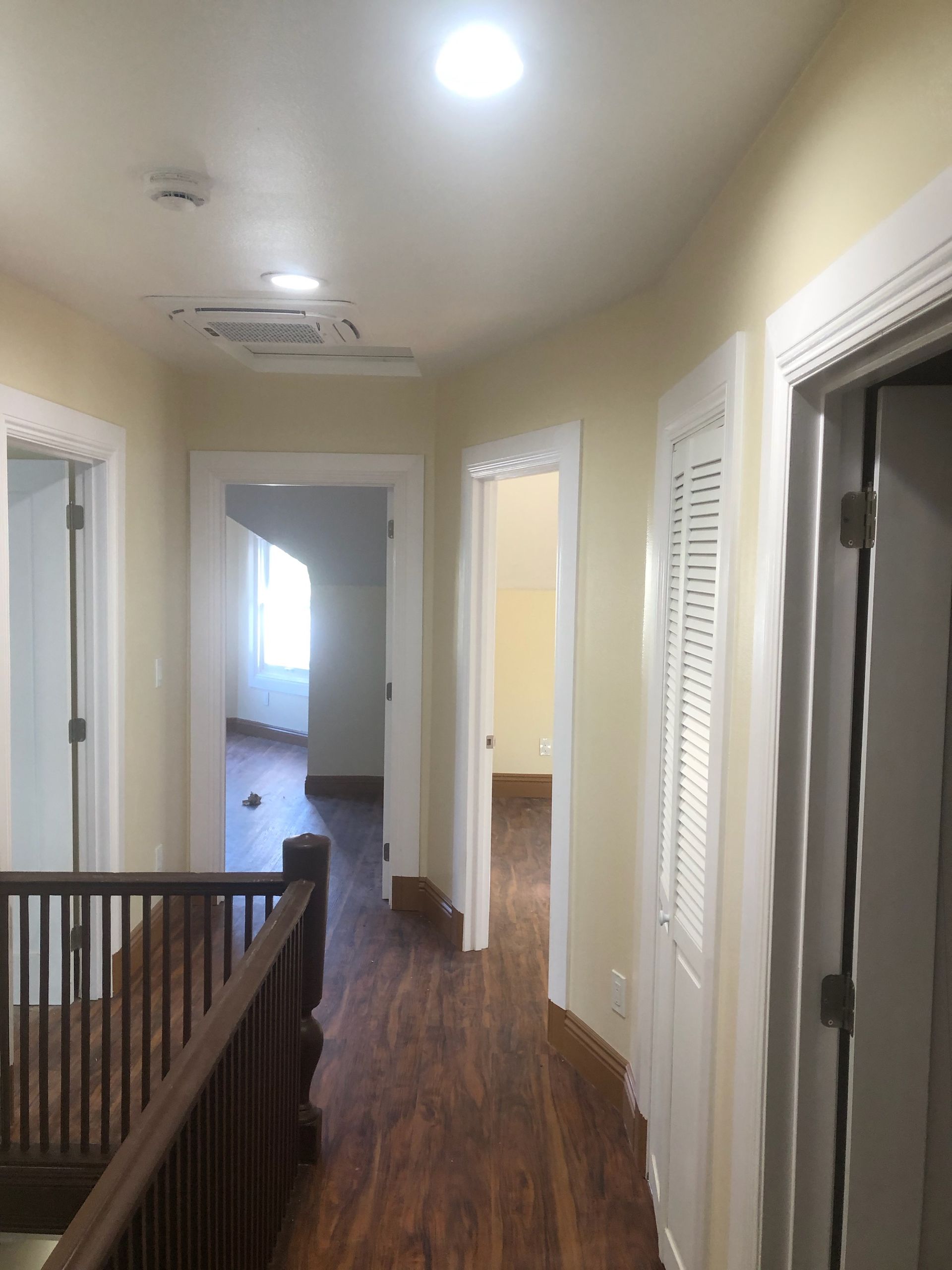 Hallway with wood floors, white walls, ceiling lights, and multiple open doorways.
